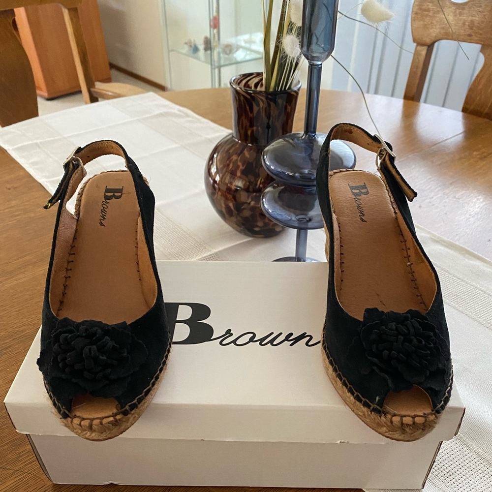 Black suede wedge shoes with a flower on top for a spring and summer look.